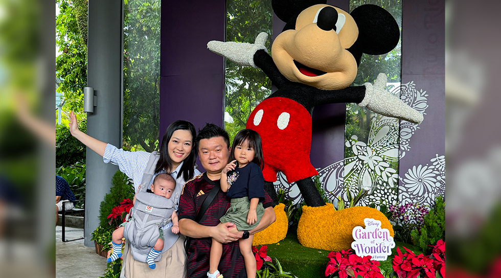 Family posing beside a large Mickey Mouse floral display at a garden attraction